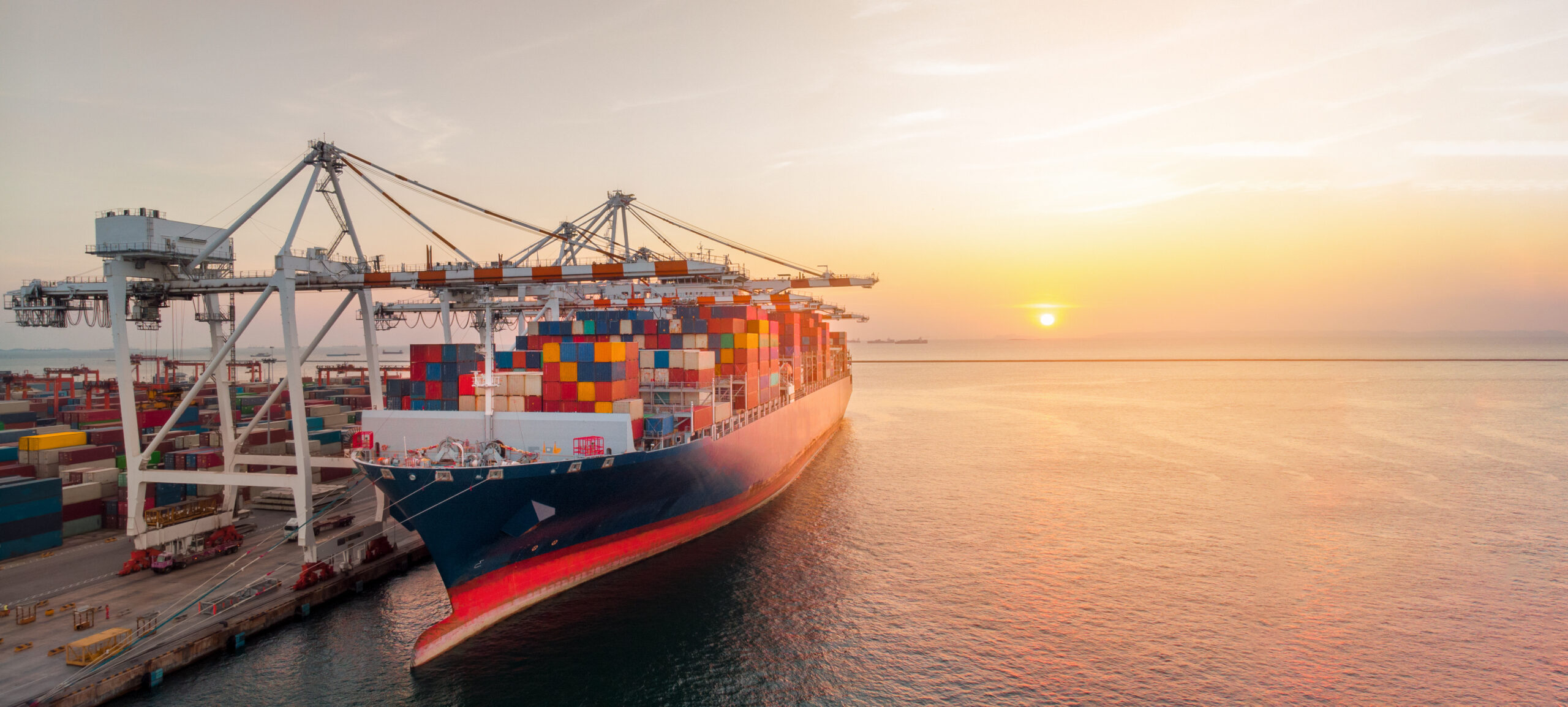 Crane loading cargo container to container ship stand by in the international terminal logistic sea port concept freight shipping by ship at sunset