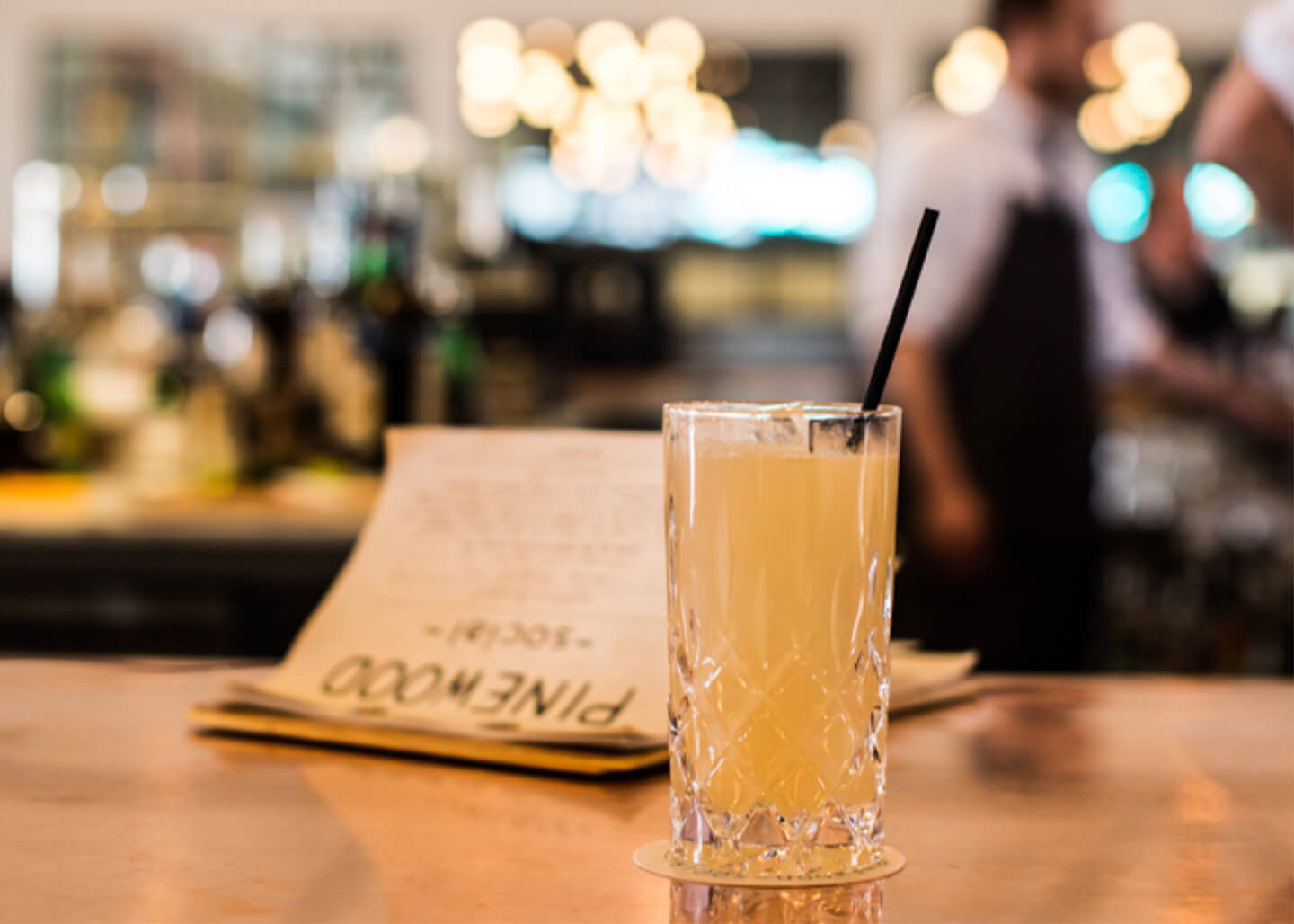 A cocktail and menu at a bar.