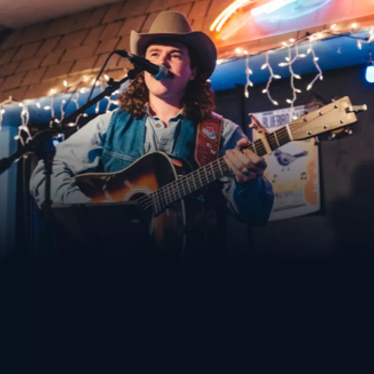 Man playing a guitar and singing during Tennessee songwriters week.